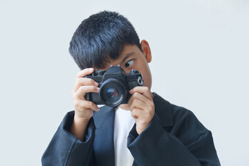 A boy in a black suit holds an old film camera in his hand, against a white background.