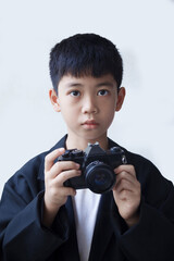 A boy in a black suit holding an old film camera in his hand, against a white background.