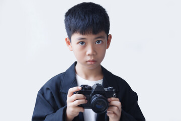 A boy in a black suit holding an old film camera in his hand, against a white background.