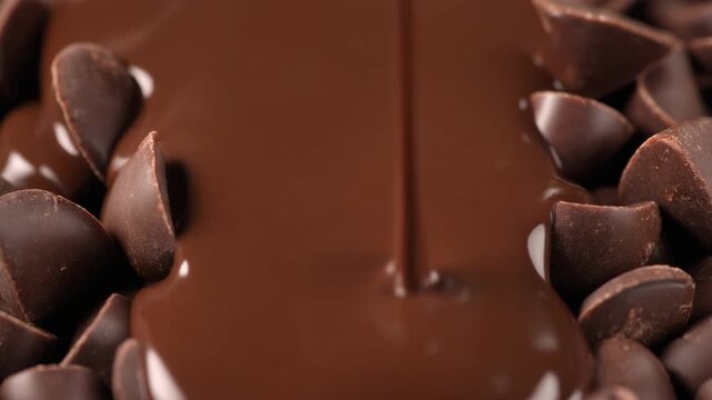 Delicious melted chocolate pouring over a pile of rich dark chocolate chips close-up, perfect for dessert and baking concepts