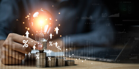 A glowing lightbulb sits on stacked coins with percentage icons and upward arrows, symbolizing financial growth, return on investment, creative strategy, and successful business innovation.