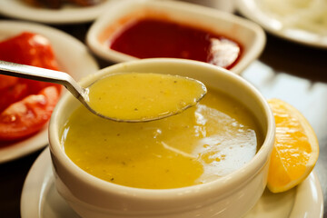 Warm and comforting lentil soup served in a white bowl with a spoon lifting portion, accompanied by lemon slice and tomato side dish in cozy restaurant atmosphere