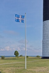 Nordic Estonian flag is flying next to S&ouml;rve lighthouse in sunny summer weather, S&otilde;rve Peninsula, Saaremaa, Estonia.