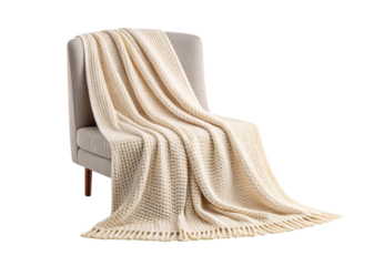 Cream colored knitted throw blanket with fringe draped over gray chair, isolated on a transparent background