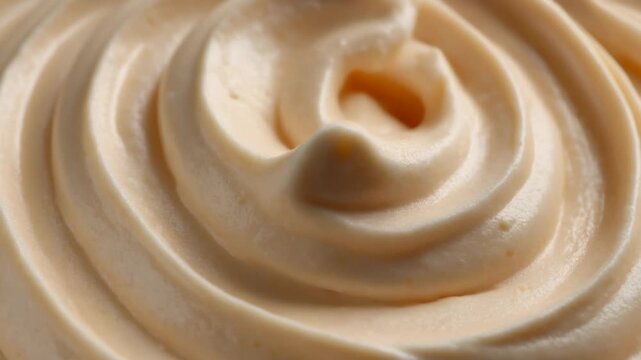 Close-up of rich creamy whipped dessert topping swirling and forming a perfect peak. Delicious light beige sweet frosting texture.