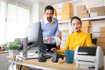 Business owner and employee labeling packages using printer and tablet in warehouse office