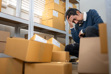 Stressed warehouse worker sitting among cardboard boxes, expressing business problem
