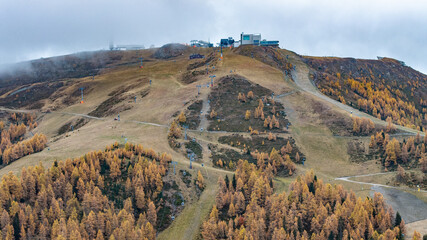 aerial landscape view of northern mountainside of Kronplatz (Plan de Corones) during autumn, with snowless ski slopes, cable car systems, houses and buildings at the summit of the mountain