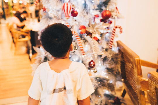 Unrecognizable young boy standing in front of white Christmas tree. Selective focus. Copy space.