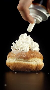 Donut topped with whipped cream shown in close-up under soft light on black background with cream spreading across surface