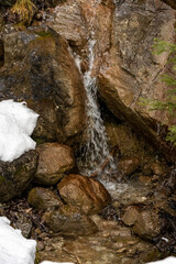 Small alpine waterfall flowing between rocks in early spring