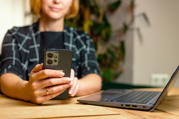 A smartphone in the hands of a woman working on a laptop.
