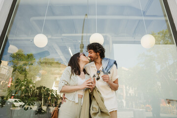 A man hugs a woman who is holding a phone while they stand and are about to kiss