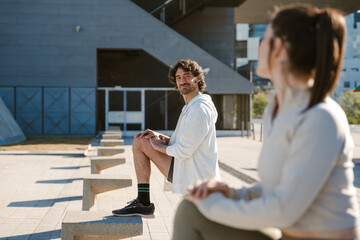 A man rests his foot on a stone stool and stretches while smiling and looking at the woman standing next to him