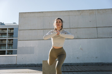 Female athlete lunges while holding her hands together in front of her and resting her foot on a...
