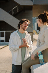 Obraz premium A man stands and smiles while talking to a woman sitting on a wall and holding a bottle