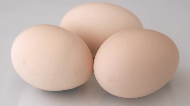 Three beige eggs arranged together on light reflective surface with smooth shell texture and natural imperfections visible in close focus
