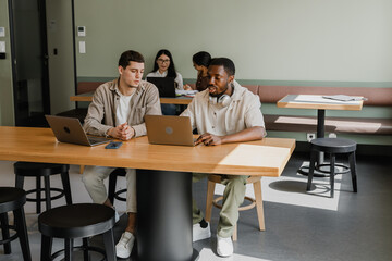 Obraz premium Two male workers are looking at a laptop and sitting at a table while one of them is talking while two female workers are behind them