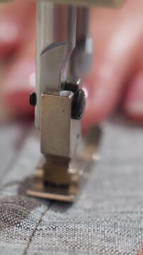 closeup sewing machine foot stitching on gray woven fabric, artisan hands guiding seamline, soft natural light, careful alignment and slow motion detail, cozy home studio atmosphere
