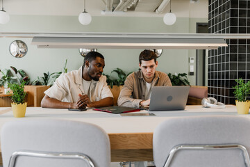 Obraz premium Two male workers sitting at a desk and looking at a laptop in front of one of them