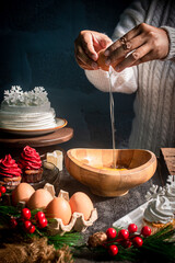 Cozy winter lifestyle scene of hands in a white knit sweater cracking an egg into a wooden bowl. Warm homemade baking atmosphere for New Year and holiday celebrations.