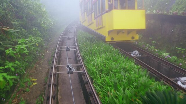 Yellow Funicular Car moving through dense Fog on Mountain Railway surrounded by lush Green Foliage in a dynamic Wide Angle view at Ba Na Hills