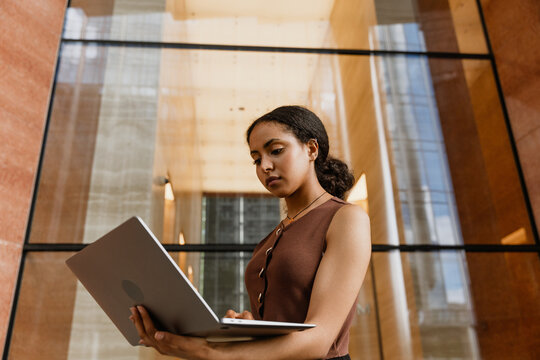 A female worker is typing on a laptop she is looking at and holding