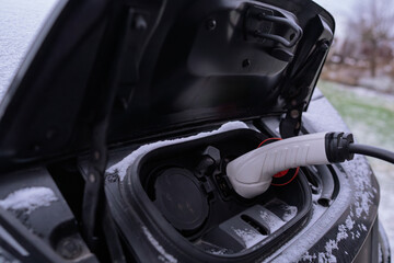 Electric vehicle charging in winter with snow on car, white charging cable plugged into EV charging port on a snowy, cold day, sustainable green energy transportation and eco-friendly mobility concept
