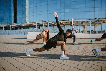 A group of three athletes rest their hands on the ground and stretch their legs while raising their other arms