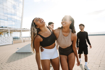 Two female athletes hug and laugh as two male athletes follow them