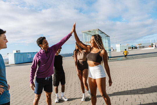 Male and female athletes high-five each other while standing next to a group of three athletes and laughing