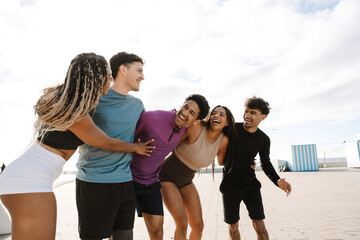 Fototapeta premium A group of five athletes laugh and hug while standing next to each other and one of them is talking