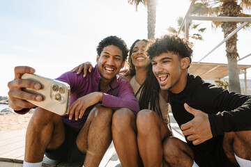 Obraz premium A group of three athletes sit and laugh while posing in front of a phone held by one of them and hugging each other