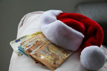 A Santa hat with a wad of Euro banknotes underneath, cash.