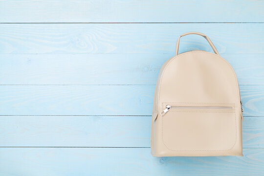 Female fashion beige backpack on wooden background, top view