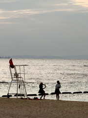 Two young women taking photos on a sandy beach near a lifeguard tower at sunset