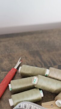 green thread spools with seam ripper scattered on wooden desk with measuring tape and buttons, seam ripper poised for undoing stitches, tailor reworking hem, upcycler restoring garment, studio repair