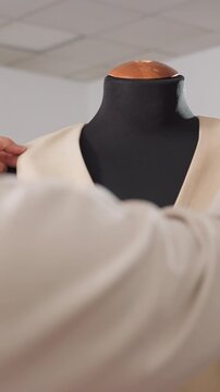 beige vest mannequin hands adjusting fabric, closeup of button detail and textured weave, calm studio lighting, seamstress inspecting seams, precision tailoring process and careful finishing