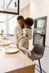 Father stands and talks while holding his daughter and they look at a baking dish on the table
