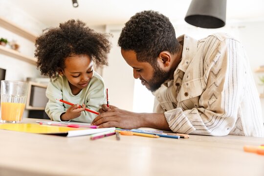 Father drawing and talking to his daughter sitting at the table while they hold pencils