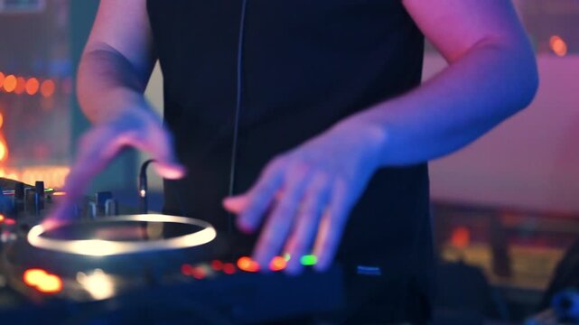 A close-up shot captures the hands of a DJ actively mixing music on a professional turntable controller, scratching a record and adjusting levels during a vibrant party or nightclub event. 