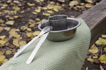 empty metal bowl and mug, with fork and knife on the table in autumn park. Picnic in nature