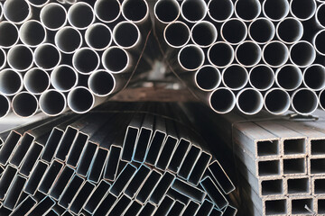 Close-up of stacked square steel hollow section profiles and round steel pipes with visible cut...