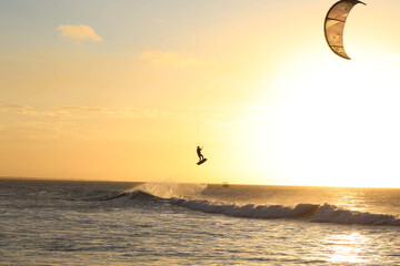 Man practicing kitesurfing in Jericoacoara beach, Brazil at sunsent time., jumping high over waves