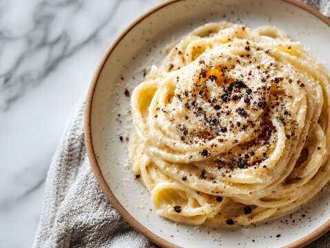 Minimalist overhead shot displays cacio e pepe pasta on a ceramic plate with a generous dusting of black pepper on a marble table.