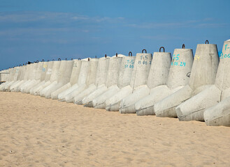 A row of concrete tetrapods stands on a sandy beach by the sea.