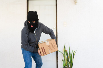 Thief in a black mask swiftly snatching a brown parcel from a doorstep, pilfering a delivered...