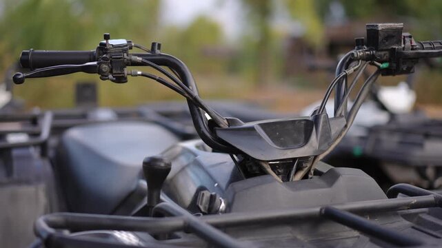 Close up of quad bike handlebars with brake levers and cables parked outdoors showing rugged design control details and off road vehicle equipment