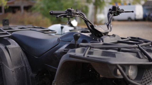 Black ATV front rack closeup showing dusty yard and rugged fender, heavy duty cargo rack, textured vinyl seat, angular headlight lens, handlebars turned