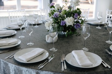 Elegant wedding table setting with grey tablecloth, white plates, and purple and white flower centerpiece